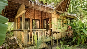 A rustic wooden house with a thatched roof, surrounded by lush greenery.