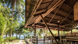 A covered outdoor seating area with concrete steps leading to a beach view, surrounded by palm trees.