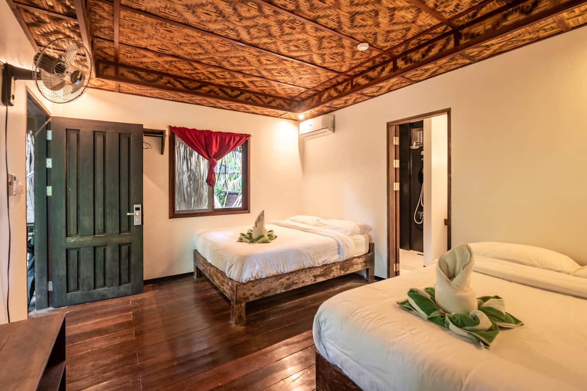 Une pièce avec un plafond en bois, un lit avec une literie blanche, une porte en bois et une fenêtre avec des rideaux rouges.