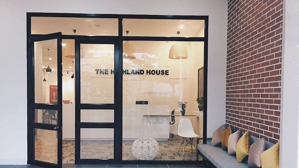 A modern interior with a glass door entrance, a seating area with cushions, and a visible sign reading "THE HIGHLAND HOUSE".