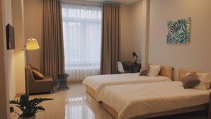 A hotel room with two beds, a desk, a chair, a lamp, and a plant.