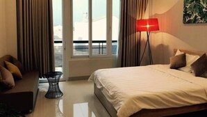 A hotel room with a bed, a desk, a chair, a window with curtains, and a painting on the wall.