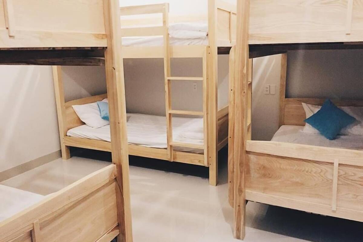 Une pièce avec trois lits superposés en bois, chacun étant équipé d’un matelas et d’oreillers. Une échelle relie le lit du milieu au lit supérieur.