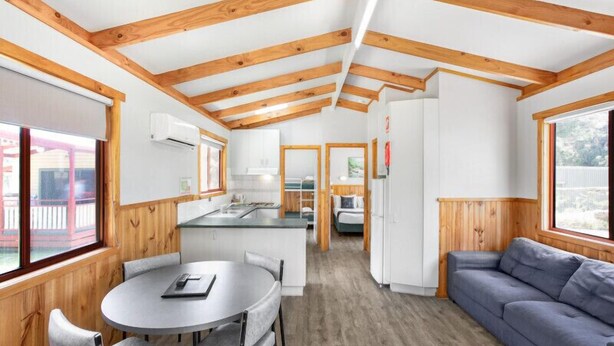 A modern interior with wooden beams, a kitchen, dining area, and a living space. - Discovery Parks - Grampians (Halls Gap)