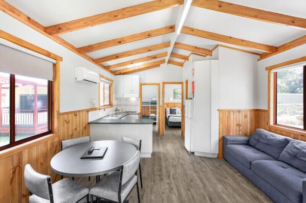 A modern interior with wooden beams, a kitchen, dining area, and a living space. - Breeze Holiday Parks - Grampians (Halls Gap)