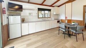 A compact kitchen with white cabinets, a built-in stove, and a dining area with a table and chairs. - Discovery Parks - Grampians (Halls Gap)