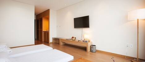 A hotel room with two beds, a wooden table, a TV, a bedside lamp, and a vase with flowers.