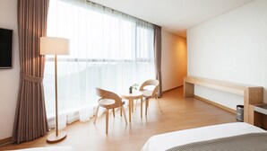 A hotel room with a bed, a desk, two chairs, a lamp, and a large window with curtains. - You Us Hotel (Seogwipo)
