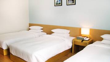 Een hotelkamer met twee enkele bedden, houten hoofdeinden, witte beddengoed, een nachtkastje met een lamp, en twee ingelijste foto’s aan de muur.