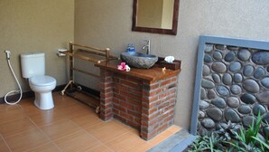 A bathroom with a toilet, a sink with a stone basin, a wooden shelf, and a mirror. - Van Karning Bungalow (Pemuteran)