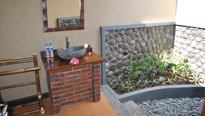 A bathroom with a stone wall, a sink with a large bowl, and a mirror above it. - Van Karning Bungalow (Pemuteran)