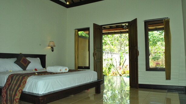 A bedroom with a bed, a nightstand, a lamp, and a window with curtains. - Van Karning Bungalow (Pemuteran)