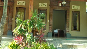 A building with a brick facade, wooden doors, and a tiled entrance area with plants. - Van Karning Bungalow (Pemuteran)