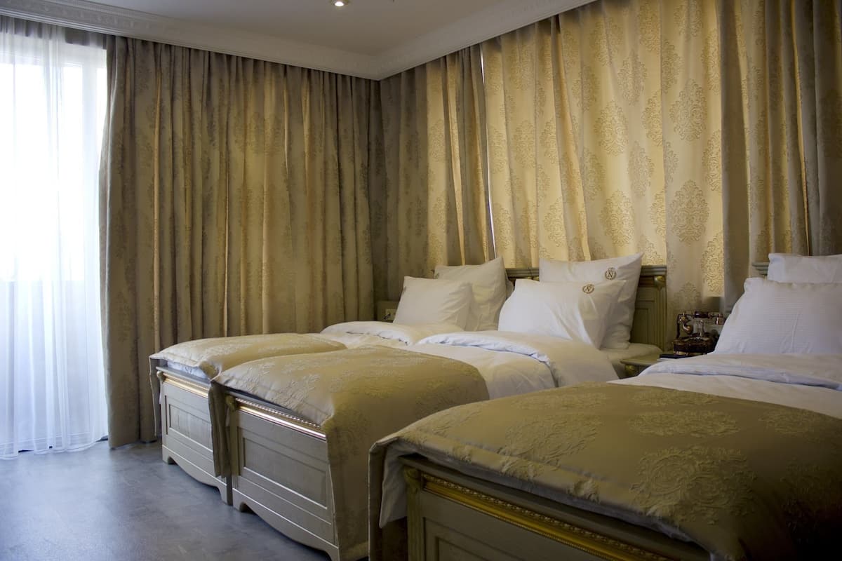 A hotel room with two beds, a large window with sheer curtains, and a classic design.