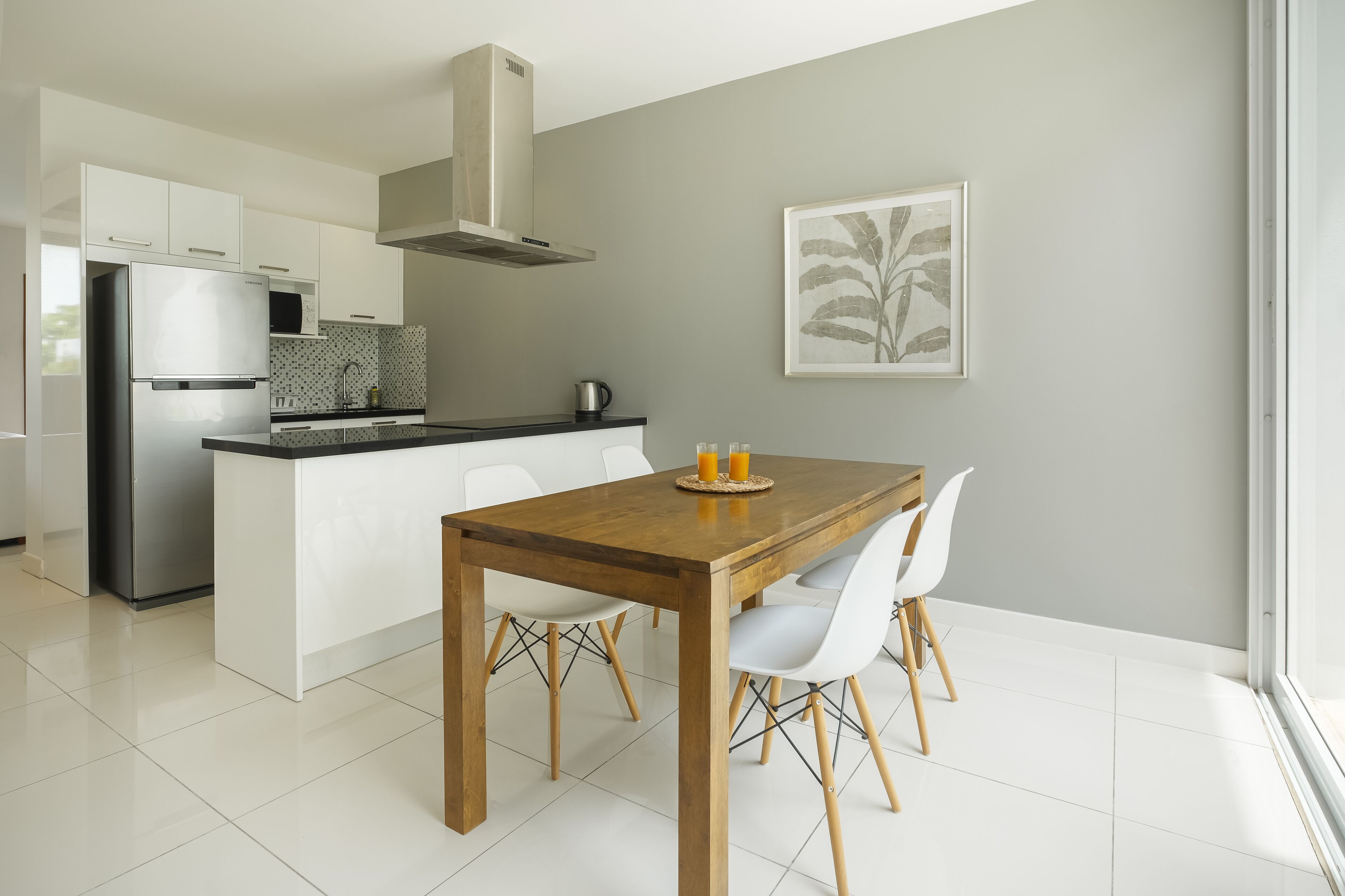 A modern kitchen with white cabinets, a stainless steel refrigerator, and a wooden dining table with white chairs.