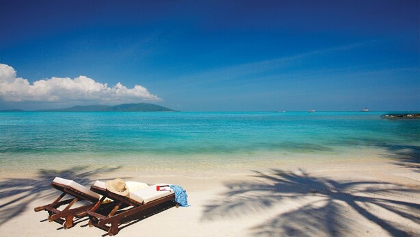 A beach with clear turquoise water, a sandy shore, and a wooden lounge chair with a hat and towel. - Horizon Residence Rentals (Koh Samui)
