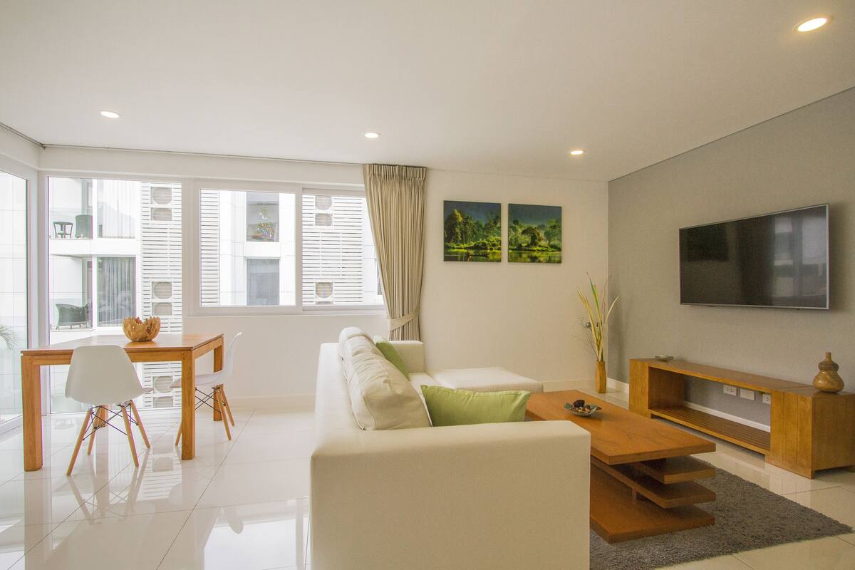A modern living room with a sofa, coffee table, TV, and a dining area with chairs and a table.