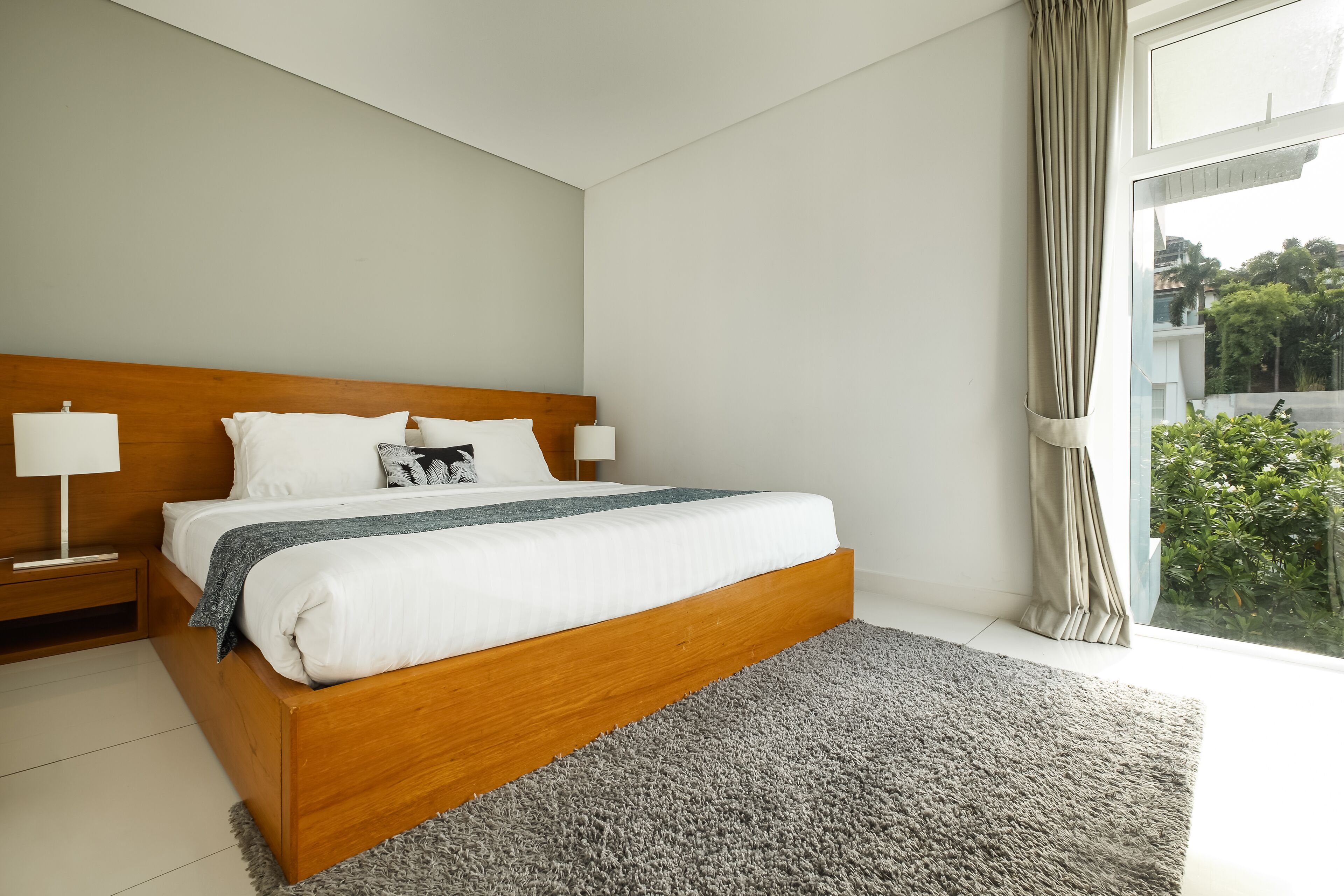 A modern bedroom with a wooden bed, white bedding, and a grey rug.
