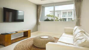 A modern living room with a flat-screen TV, a wooden console table, a white sofa, and a woven rug.