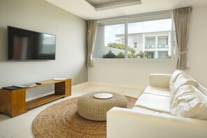 A modern living room with a flat-screen TV, a wooden console table, a white sofa, and a woven rug.