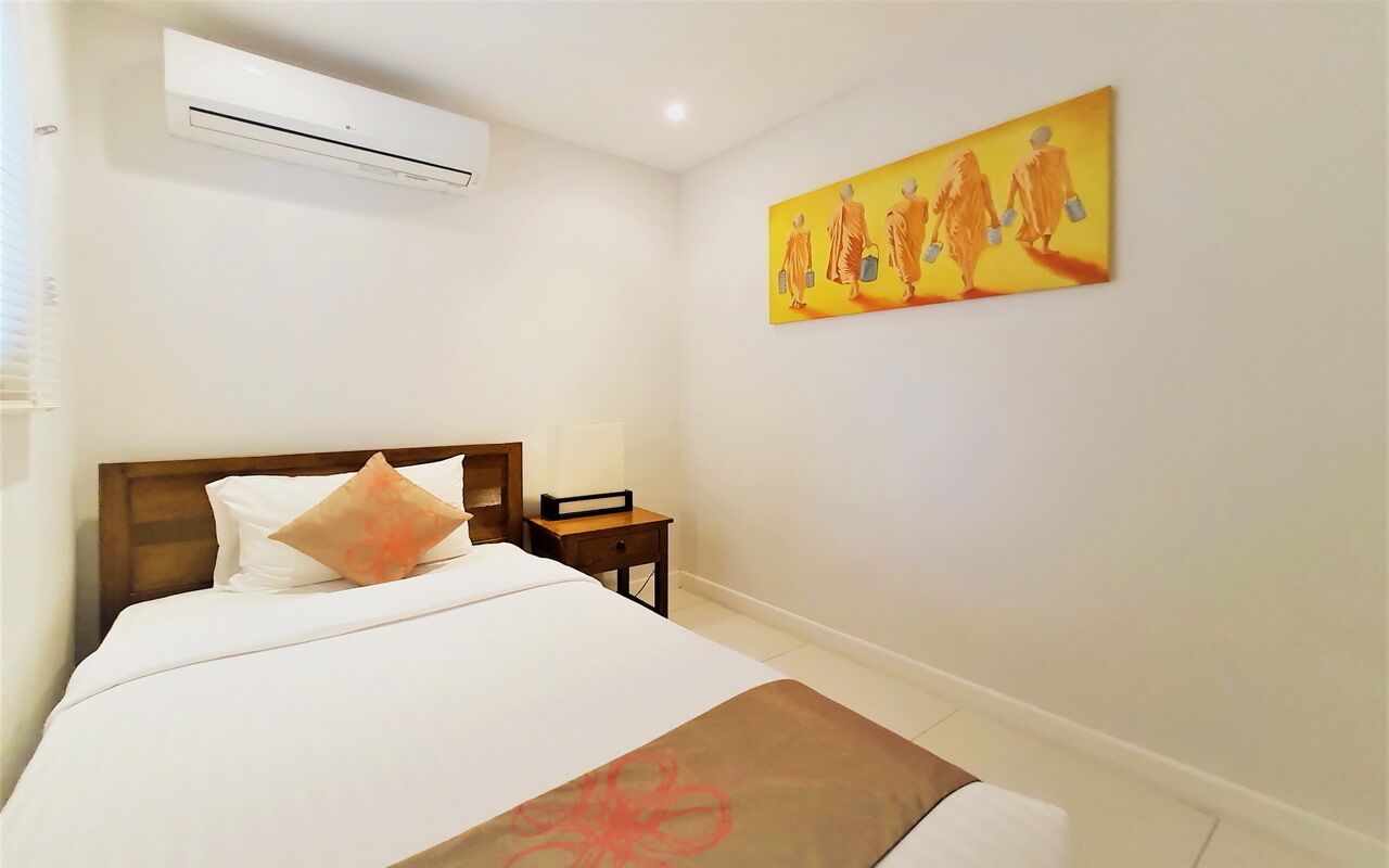 A hotel room with a bed, a nightstand, an air conditioner, and a painting on the wall.