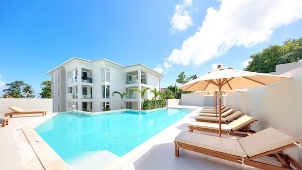 A modern pool area with a clear blue pool, lounge chairs, and a large umbrella.