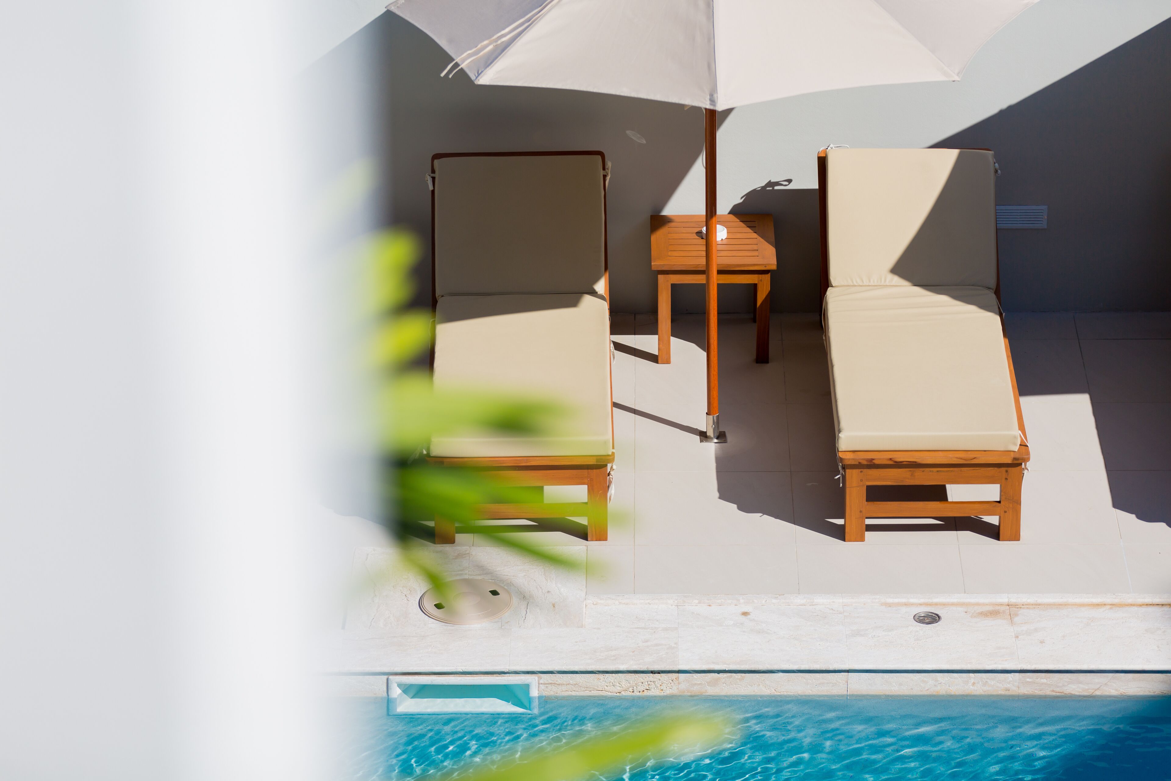 A poolside area with two lounge chairs and a table under a large umbrella.