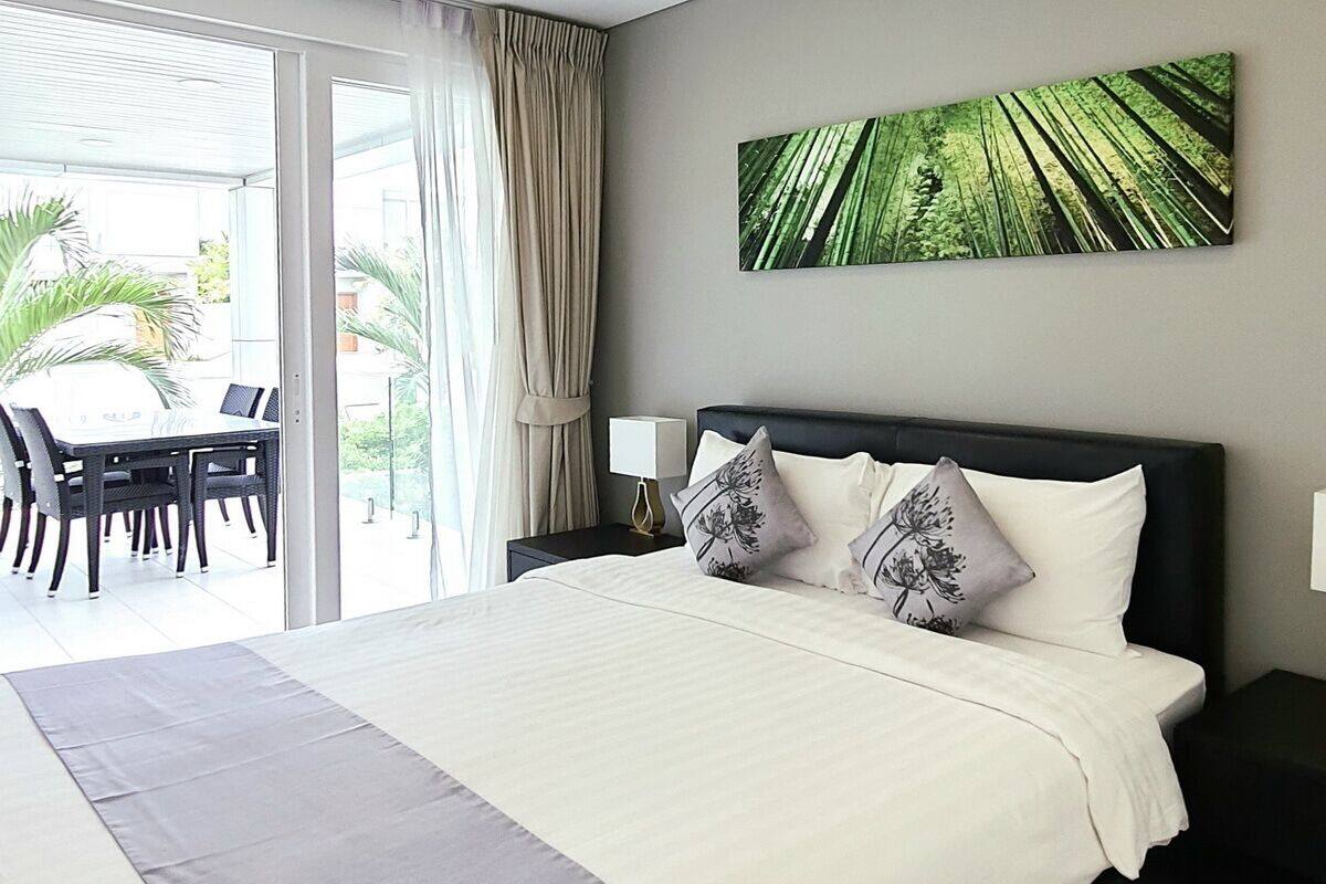 A hotel room with a large bed, a view of the outdoors, a dining area with chairs, and a painting on the wall.