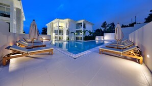 A modern pool area with lounge chairs and umbrellas, surrounded by a white building with balconies.