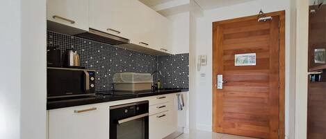 Une cuisine moderne avec des meubles blancs, un plan de travail noir, un four à micro-ondes et un four traditionnel.