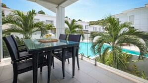 A glass-top table with wicker chairs, a pool, and white buildings in the background. - Horizon Residence Rentals (Koh Samui)