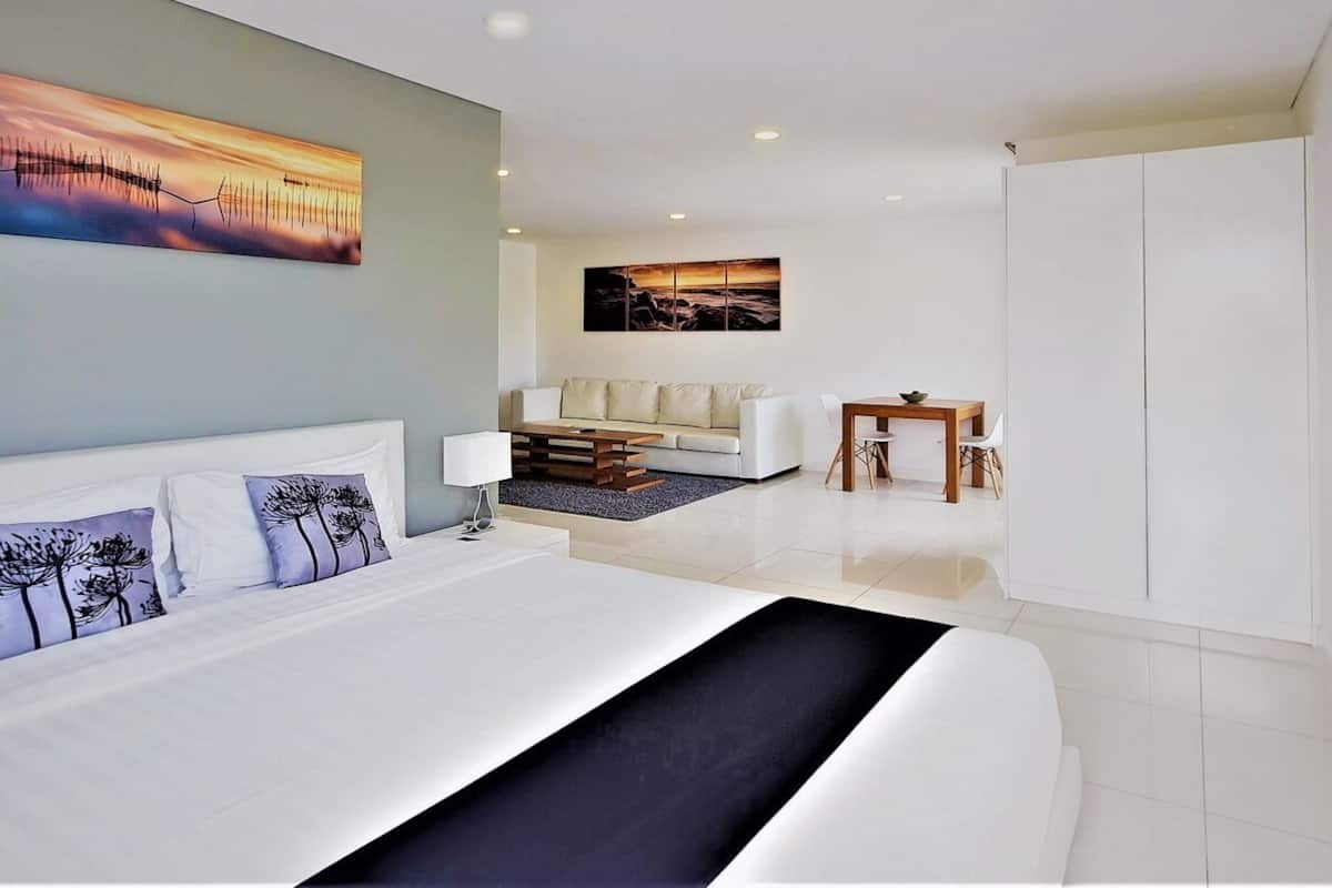 A modern hotel room with a large bed, a sofa, a small table, and artwork on the walls.