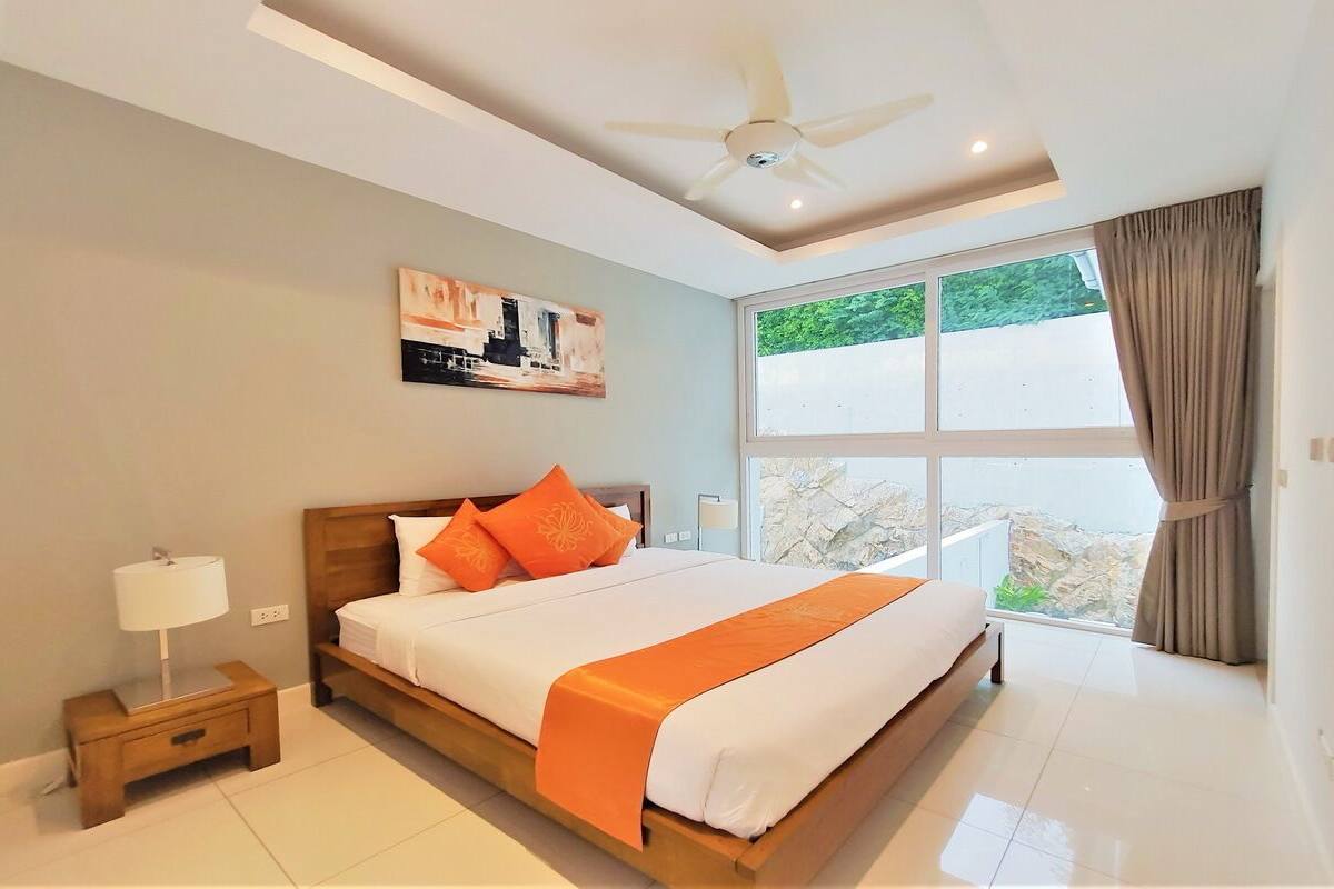A modern hotel room with a large bed, a ceiling fan, a window with a view, and a painting on the wall.