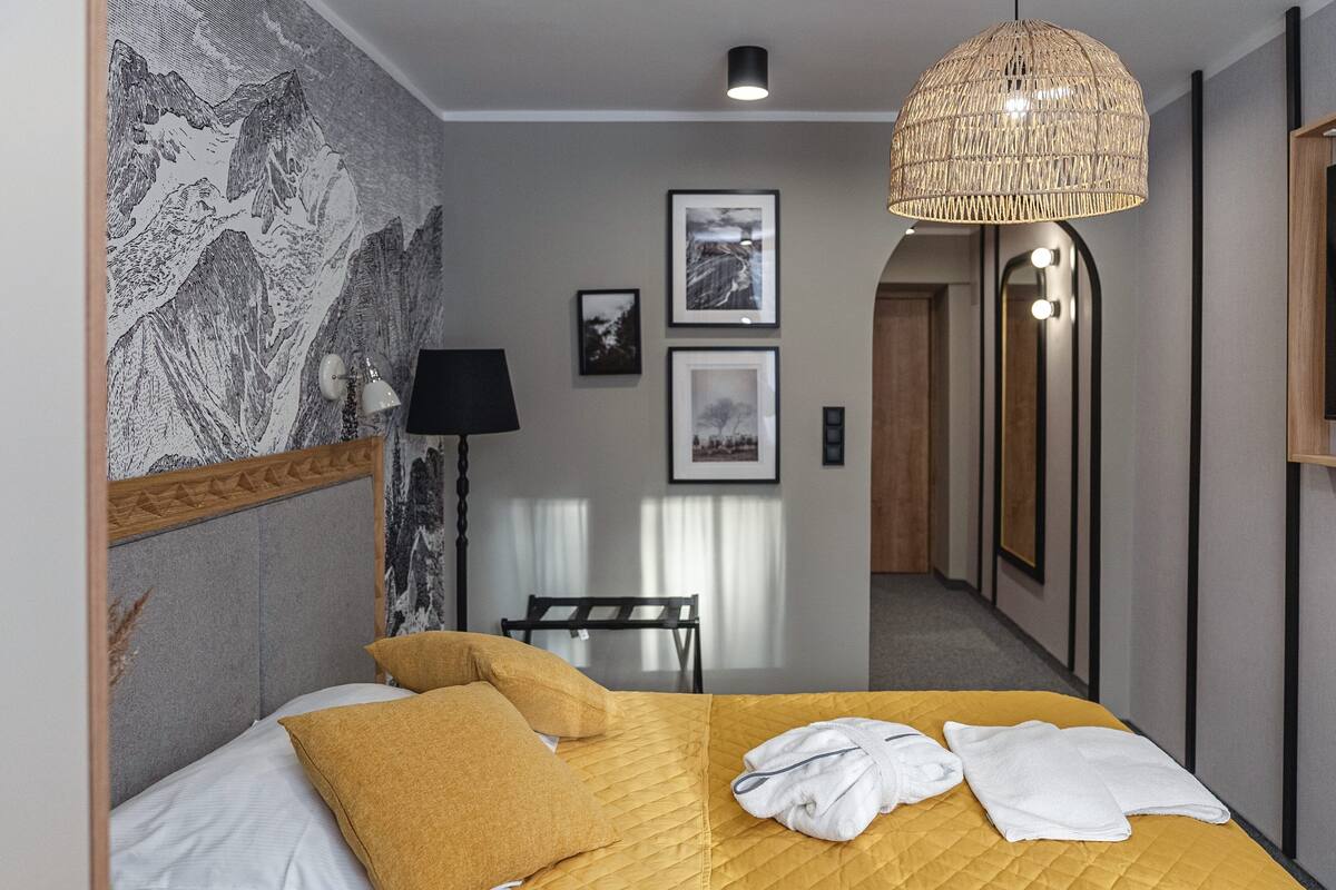 Habitación de hotel con cama, lámpara de noche, lámpara colgante y cuadros en la pared.