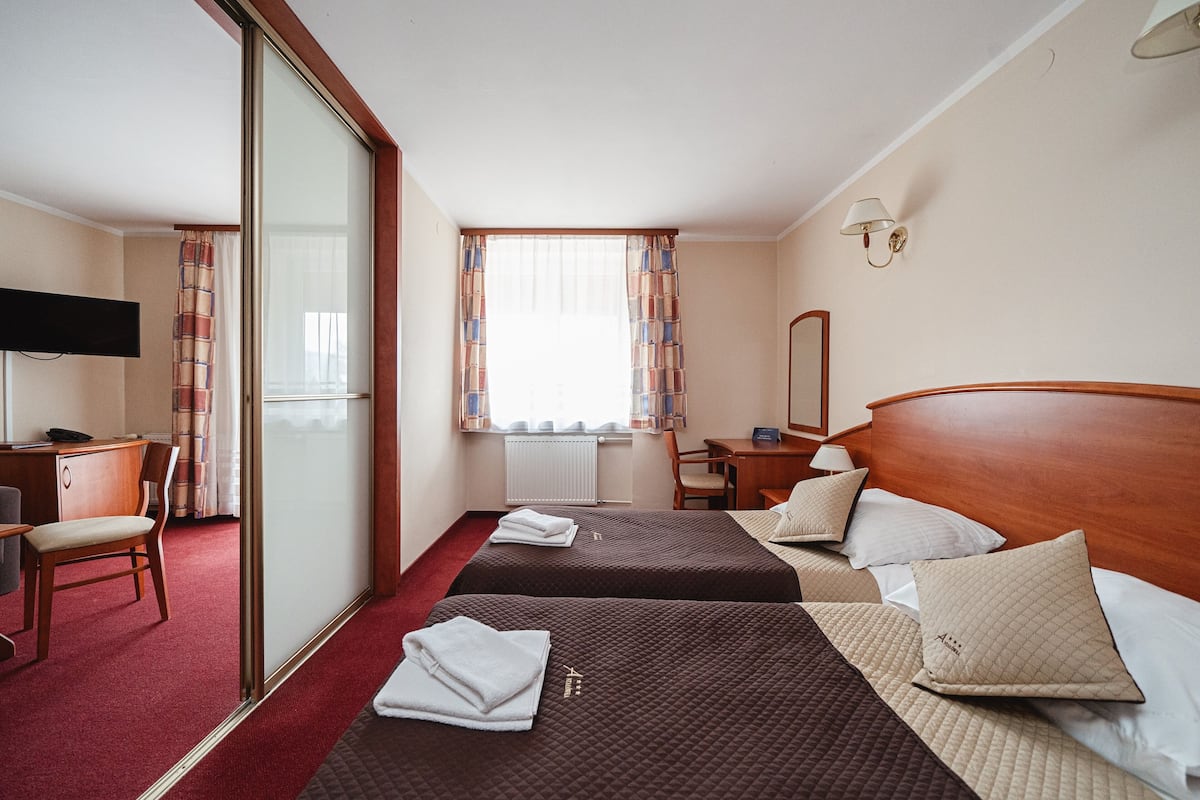 Habitación de hotel con dos camas, un escritorio, una silla, un televisor y una ventana con cortinas.