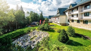 Un hotel con fachada de piedra, varios balcones y un jardín bien cuidado con un estanque.