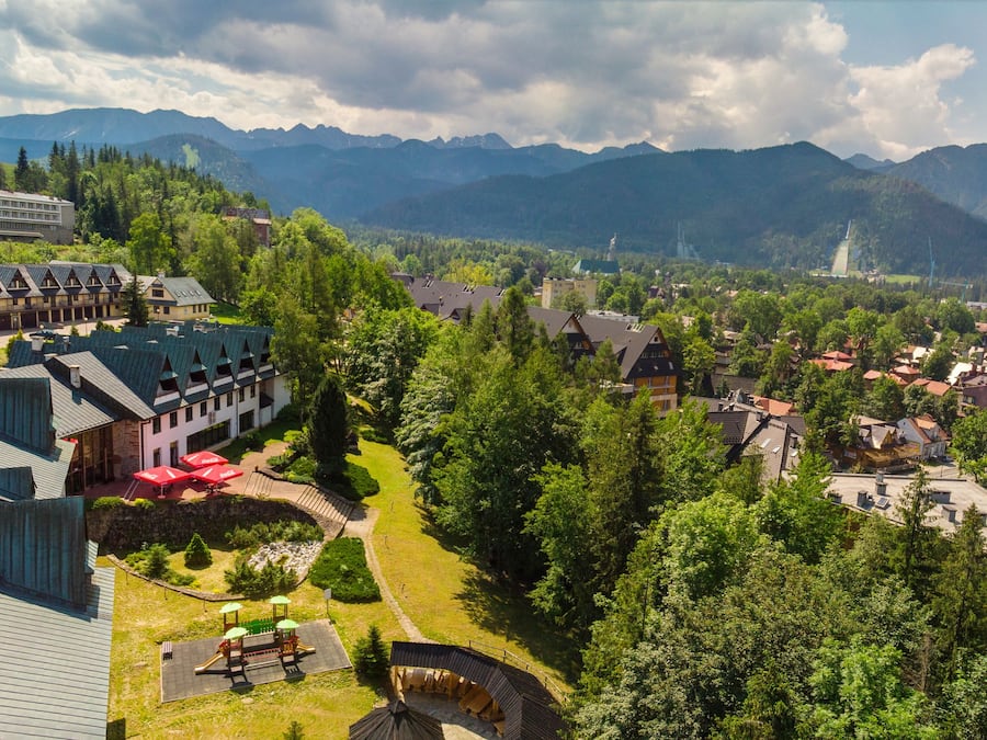 A mountain resort with chalet-style buildings, a playground, and a view of the surrounding mountains.
