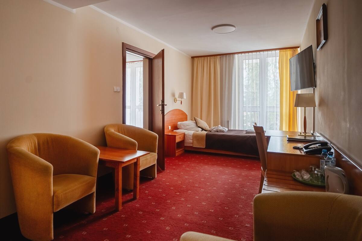 Habitación de hotel con cama, dos sillones, un escritorio, una lámpara y un televisor.