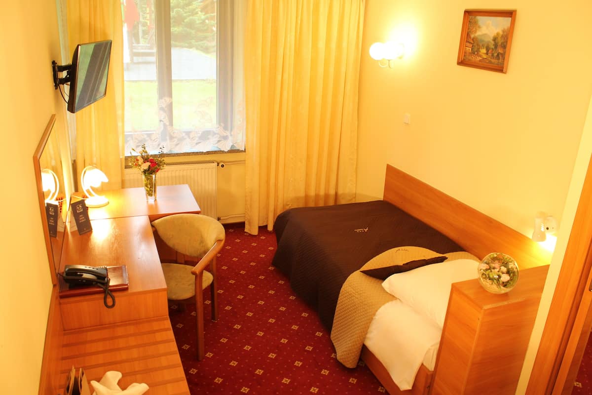Habitación de hotel con cama, escritorio con teléfono, silla, ventana con cortinas y un cuadro en la pared.