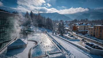 A winter scene with a snow-covered pool, buildings, and mountains in the background.