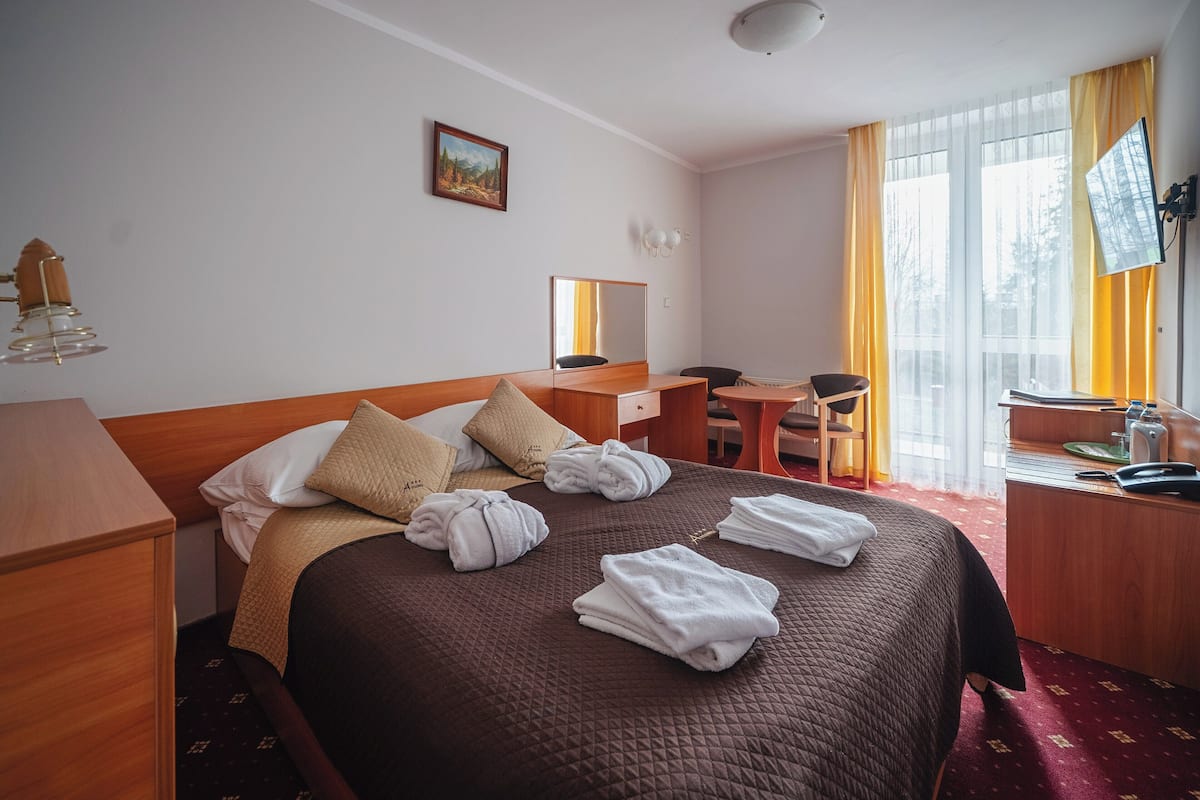 Una habitación de hotel con una cama grande, un escritorio, una silla, una mesita, un espejo y una ventana con cortinas.