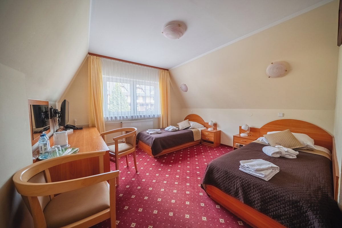 Habitación de hotel con cama, escritorio, silla, televisor y ventana con cortinas.