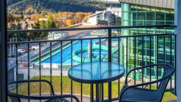 A balcony with a view of a swimming pool, a building with large windows, and a mountainous landscape.