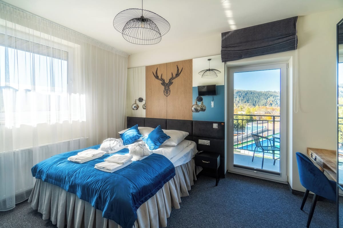Habitación de hotel con una cama grande, un escritorio, una silla, un televisor y un balcón con vista a la piscina.