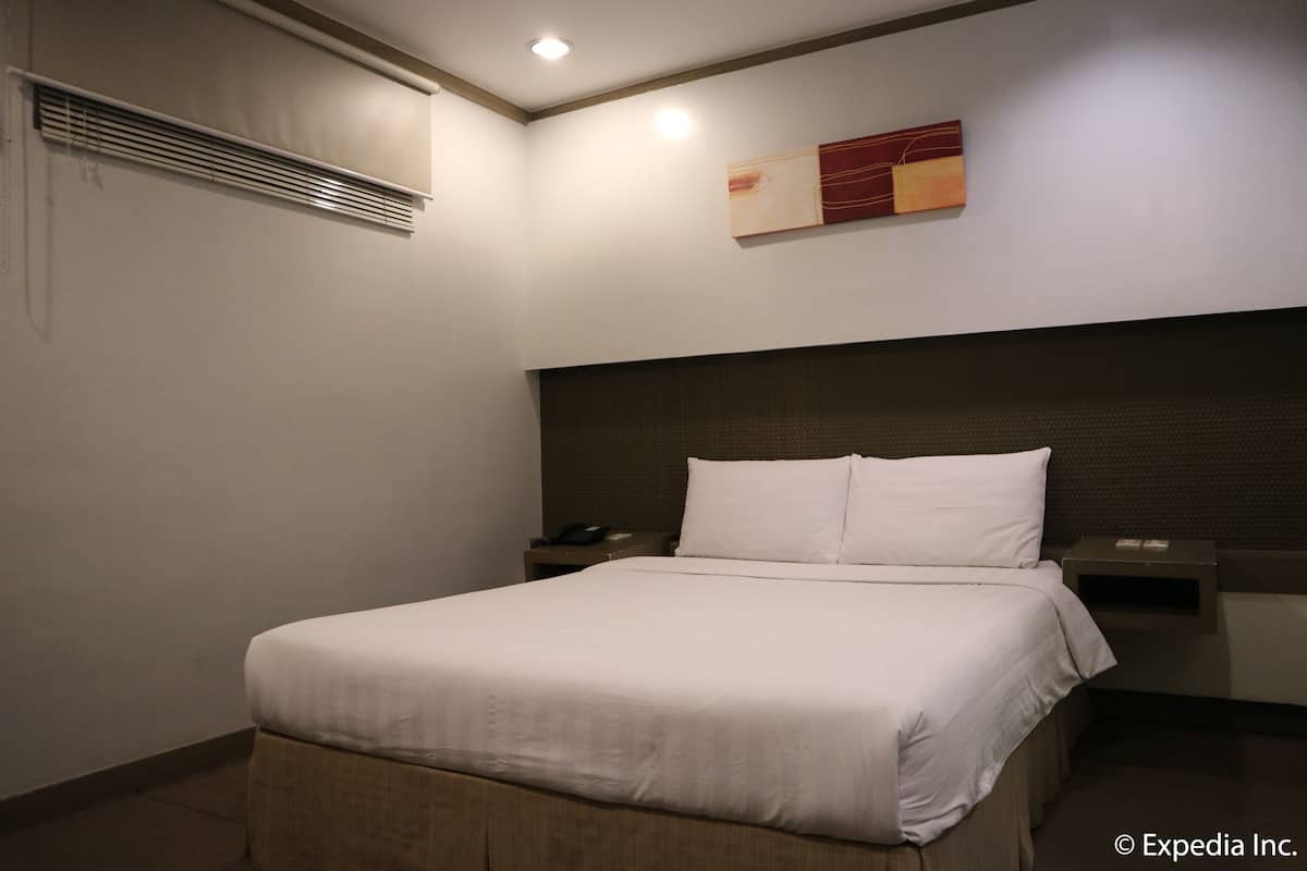 A hotel room with a bed, bedside tables, a wall-mounted artwork, and a ceiling light.