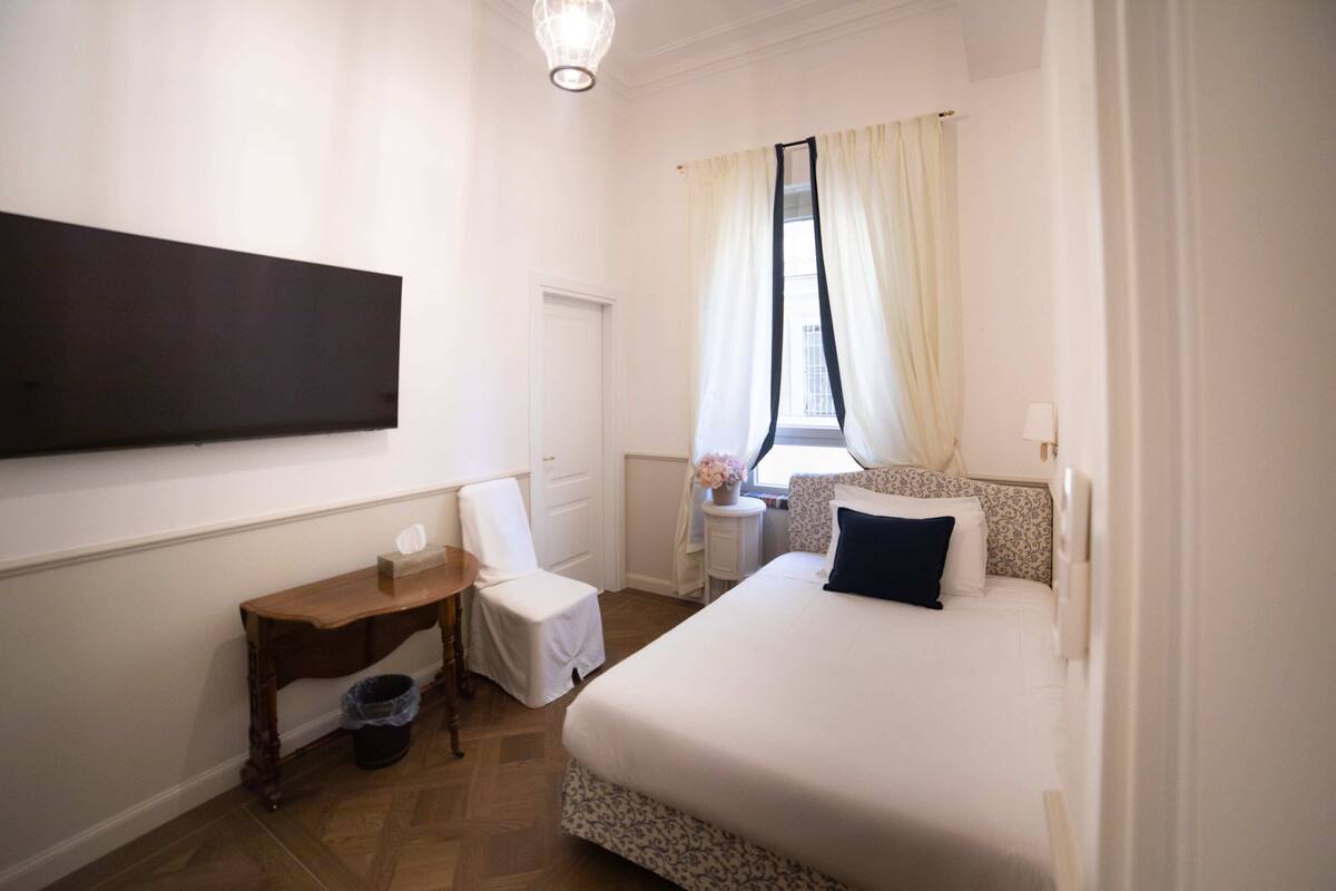 A hotel room with a bed, a chair, a small table, and a TV mounted on the wall.