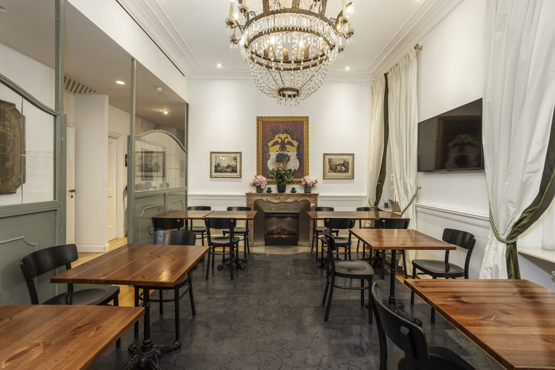 A dining area with wooden tables and chairs, a chandelier, and a fireplace.