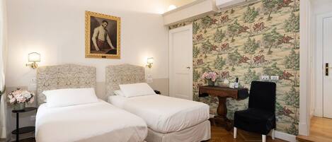 A hotel room with two beds, a portrait on the wall, a floral wallpaper, and a wooden floor.