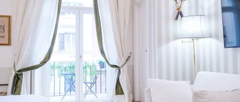 Una habitación de hotel con cama, ventana con cortinas, lámpara y una raqueta de tenis en la pared.