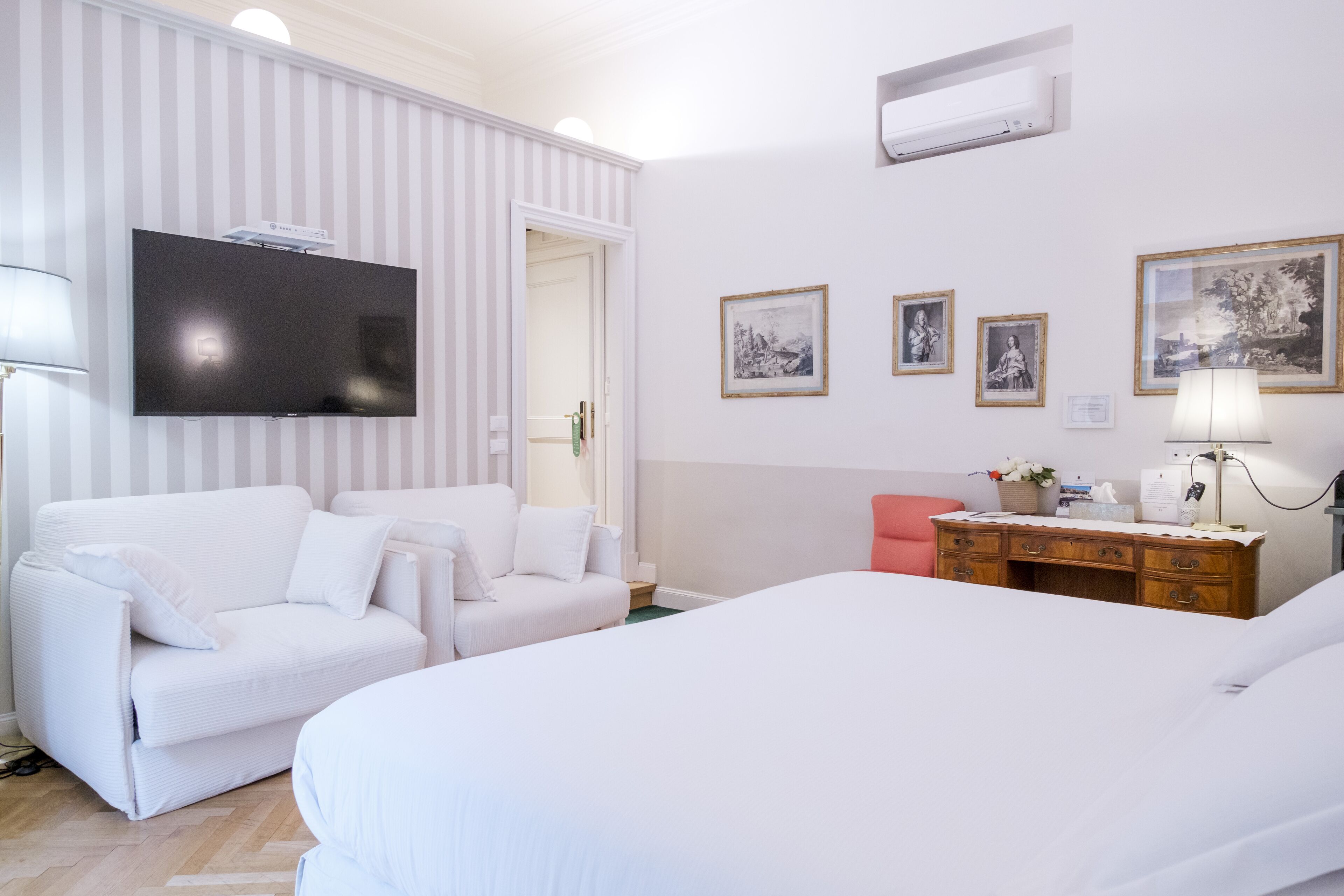 Une chambre d’hôtel avec un grand lit, un canapé blanc, un bureau en bois et un téléviseur à écran plat fixé au mur.